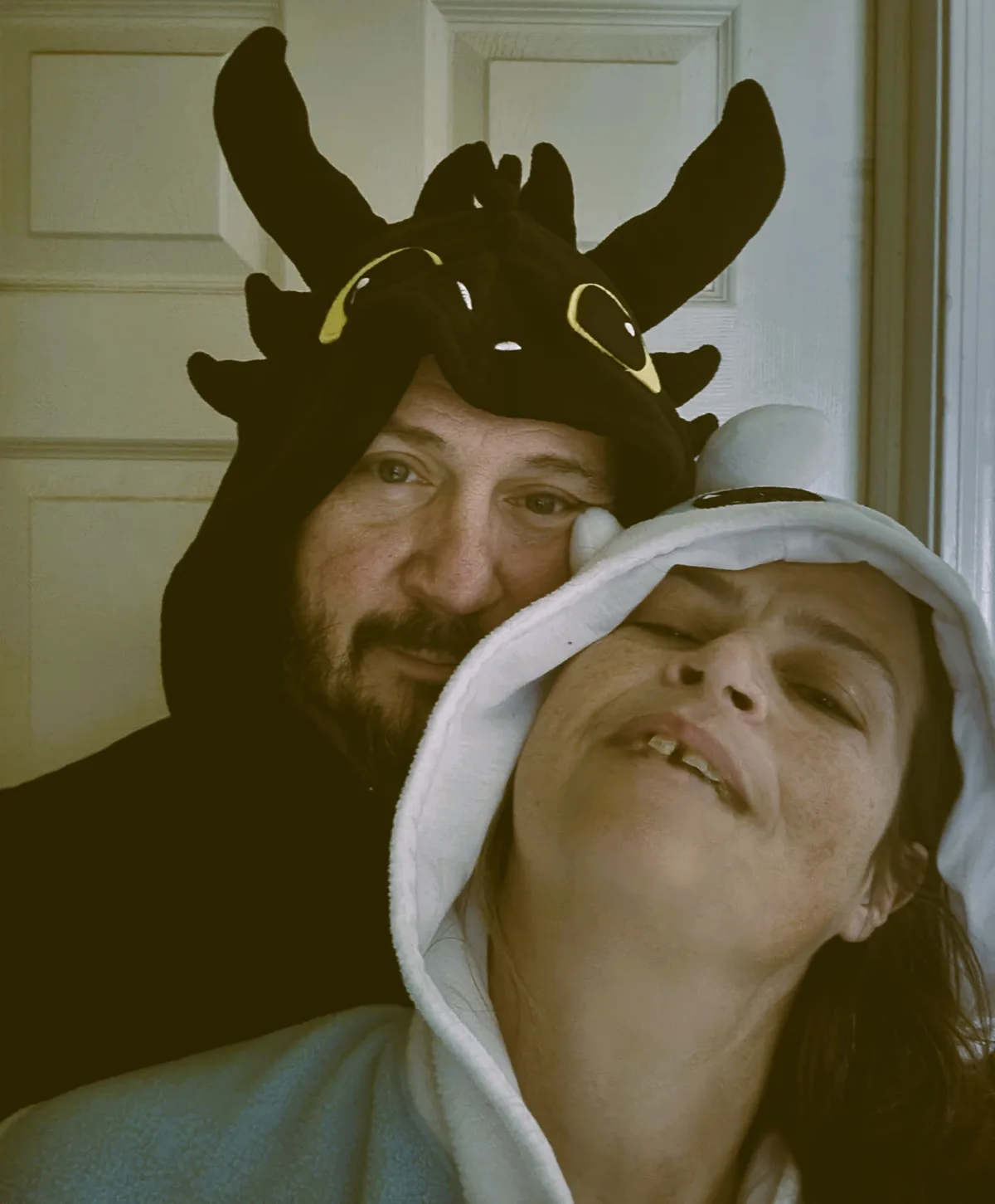 A man wearing a black Toothless dragon hooded costume leans close to a woman wearing a white, fluffy hooded costume with a…