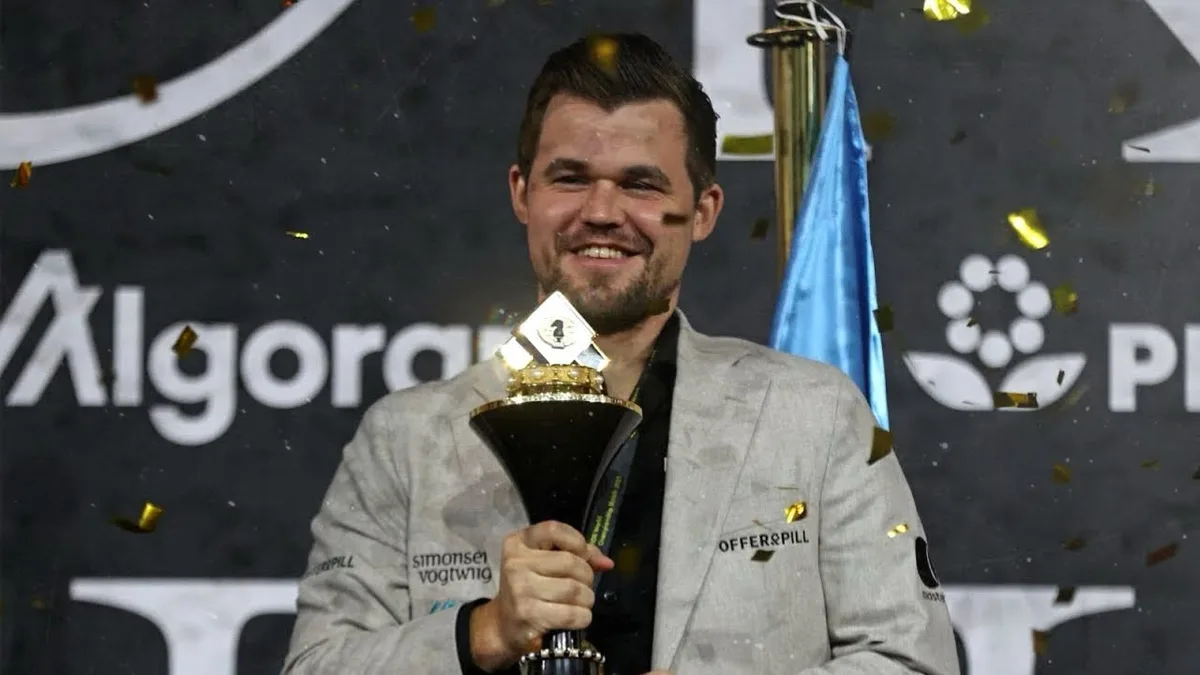 a man in a grey suit holding a large trophy with gold confetti falling around him, smiling broadly. The background has logos…