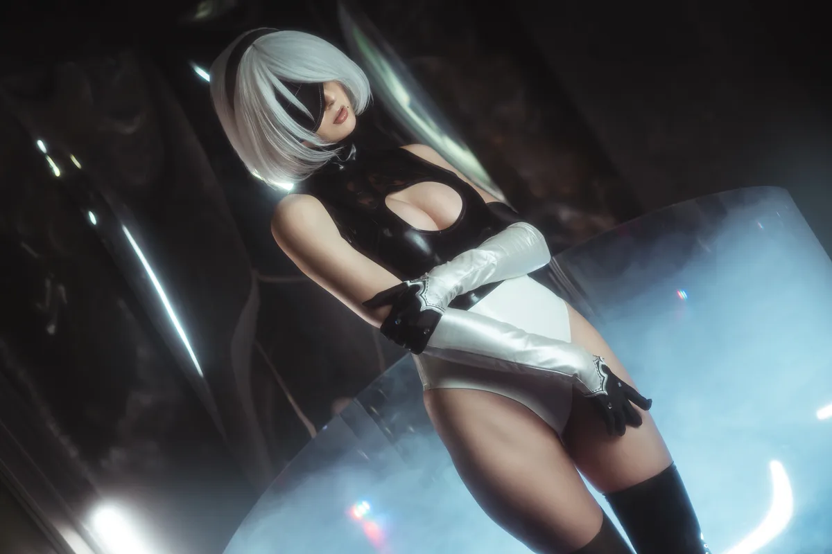 A person in a detailed cosplay of the character 2B from NieR: Automata, wearing her signature white bob wig, black eye…
