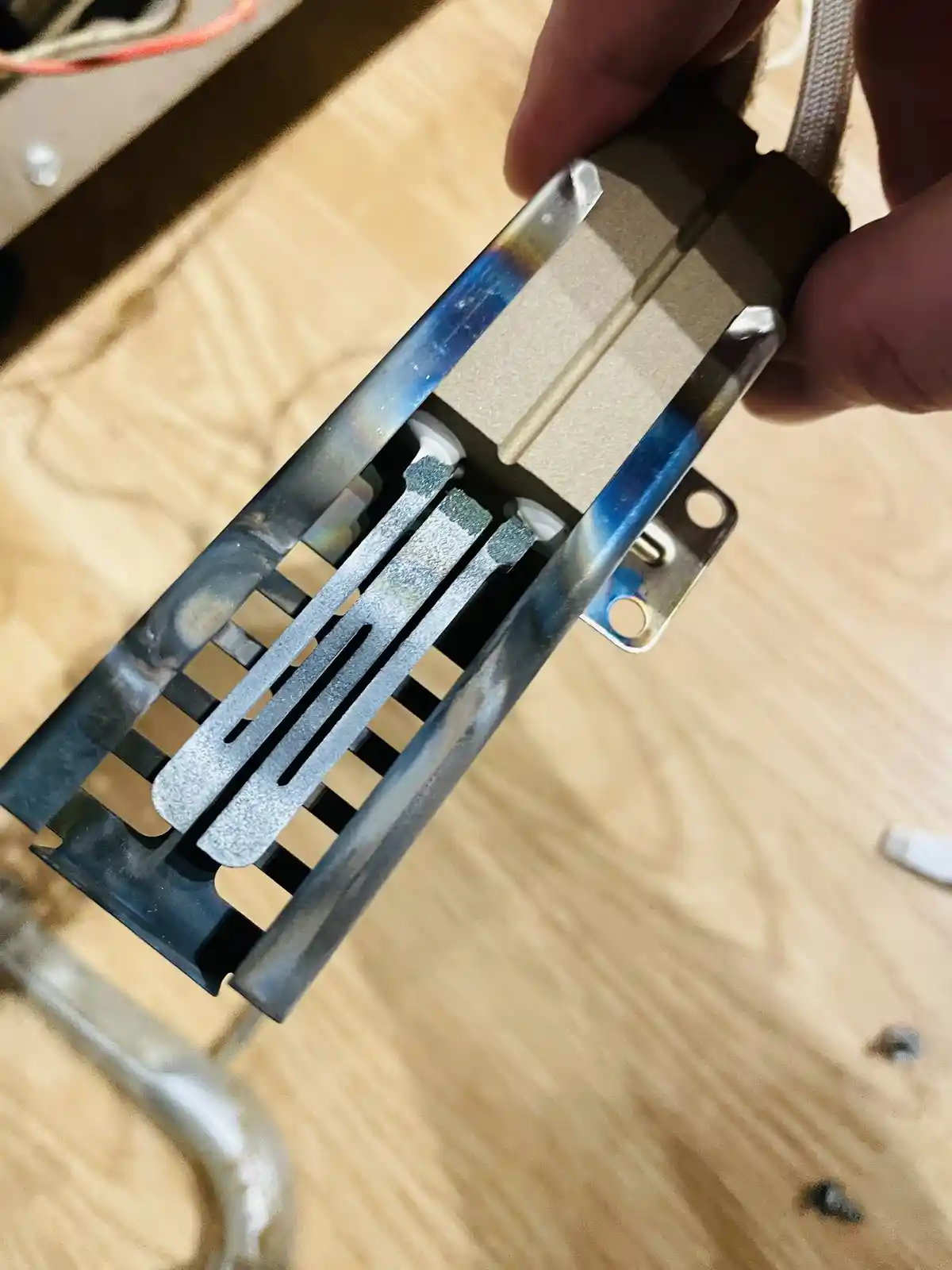 A close-up photo shows a person's hand holding a metal computer component, likely a CPU cooler or heatsink bracket, with…