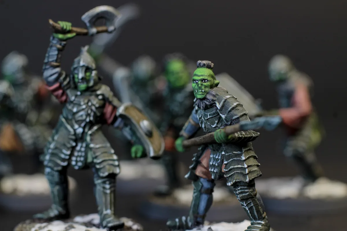 A close-up photograph of several painted miniature orc figurines in battle poses, with one in the foreground looking…