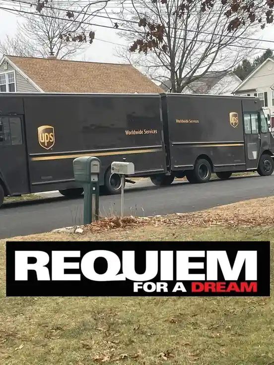 A black UPS delivery truck is parked on a residential street next to a mailbox, with bare trees and houses in the…