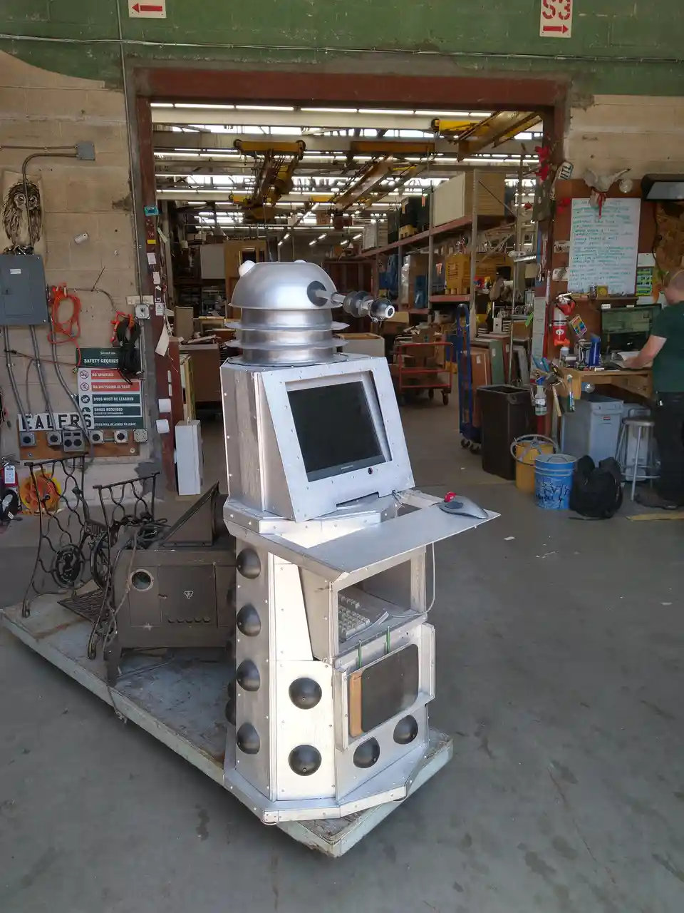 A homemade Dalek from Doctor Who, constructed from metal and an old computer monitor, stands on a wooden pallet in a…