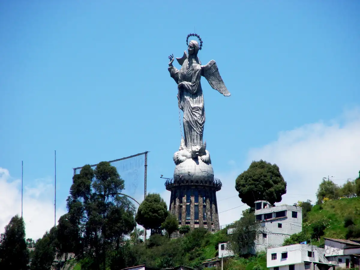 A large, weathered statue of an angelic figure with wings, a halo, and a chain, standing atop a globe-like pedestal…