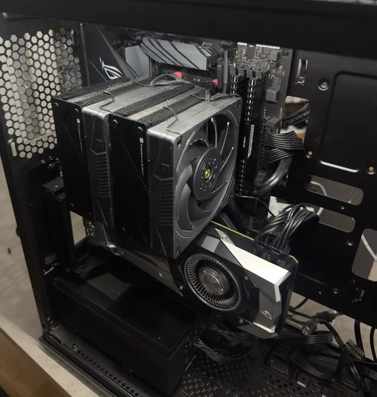 A close-up photo of the inside of a black computer case showing a large black CPU cooler with multiple heat pipes and a fan…