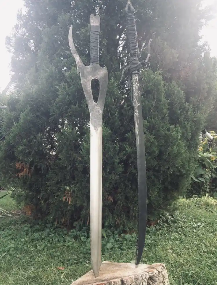Two custom-made fantasy swords stand upright in a grassy outdoor area, leaning against a tree stump. The sword on the left…
