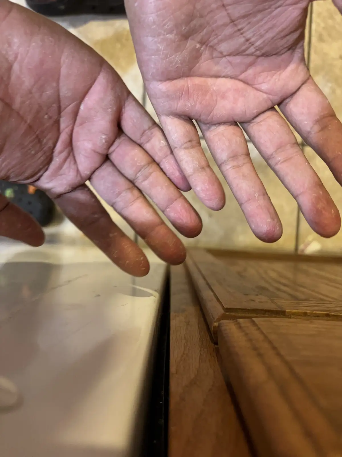 A close-up shot shows two hands covered in white dust or flour, hovering over a wooden surface and a countertop. The…
