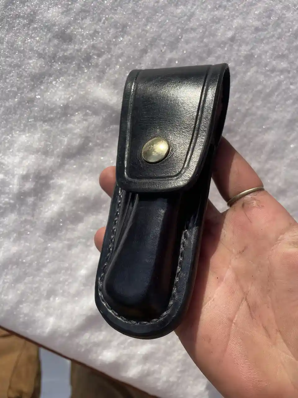 A hand holds a black leather holster with a brass snap button against a snowy background. The text overlaid on the image…