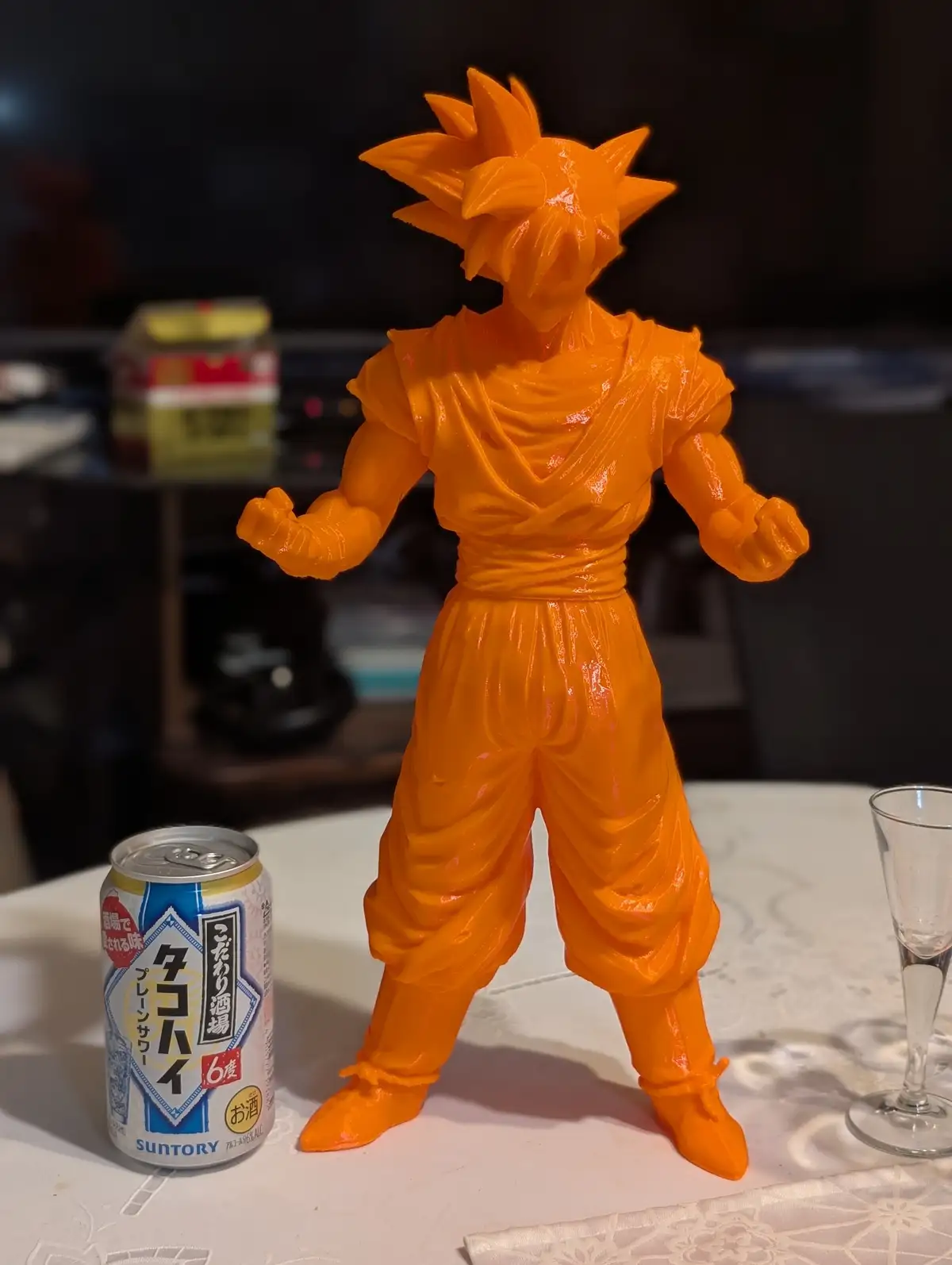 A bright orange, monochromatic figurine of the anime character Goku in his Super Saiyan form stands on a white tablecloth…