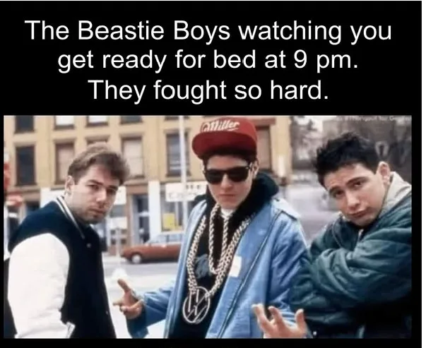The image shows three men, identified as The Beastie Boys, standing outdoors on a city street. The central figure wears a…