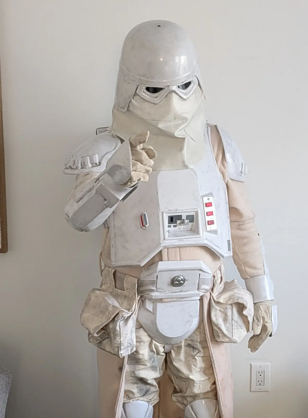 A person in a full, weathered snowtrooper costume from Star Wars stands indoors against a plain wall, pointing at the camera…