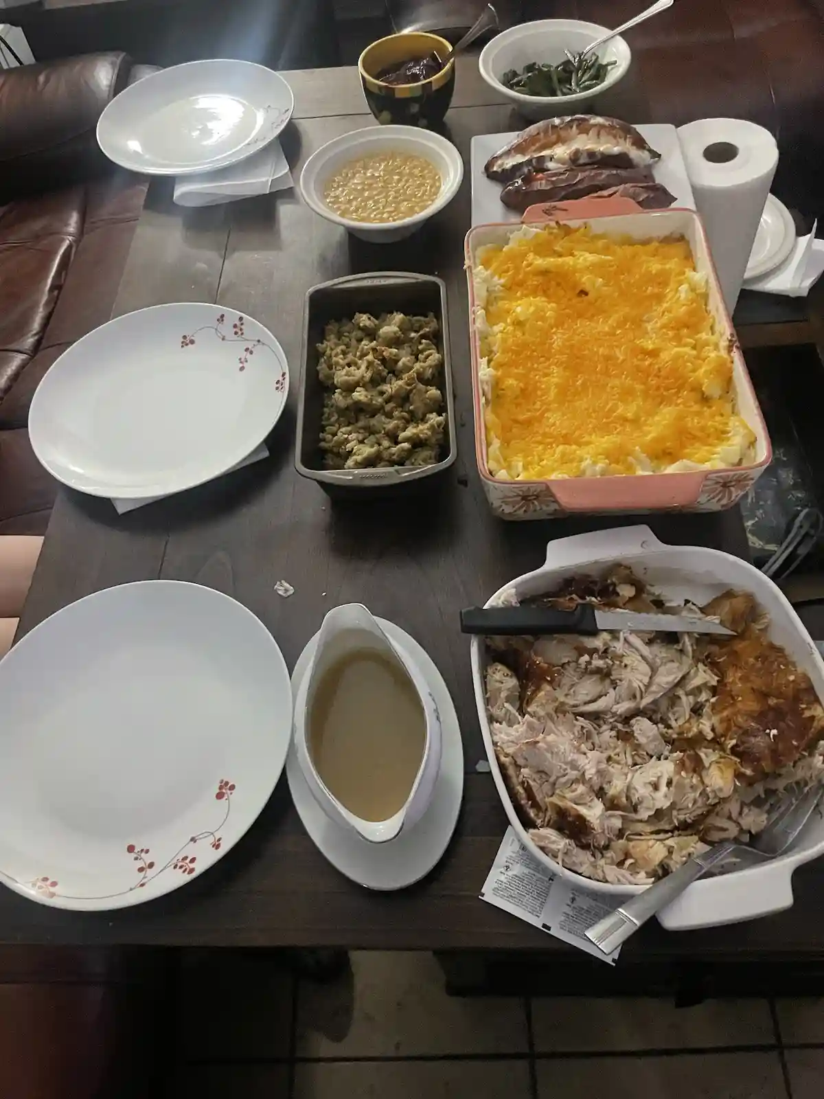 An overhead photo shows a dark wooden table laden with a large, elaborate Thanksgiving-style meal, including a casserole…