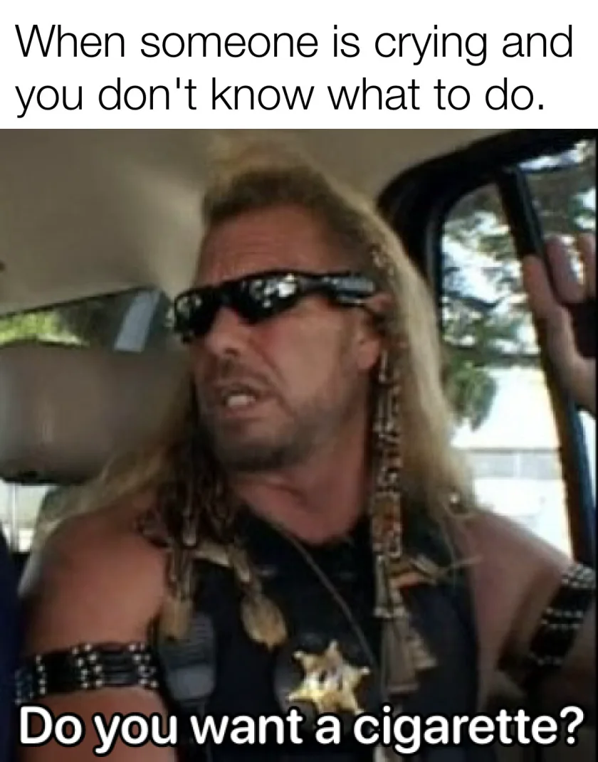 A man with long blonde hair, sunglasses, and a sheriff's star on his vest is inside a vehicle, looking concerned and…