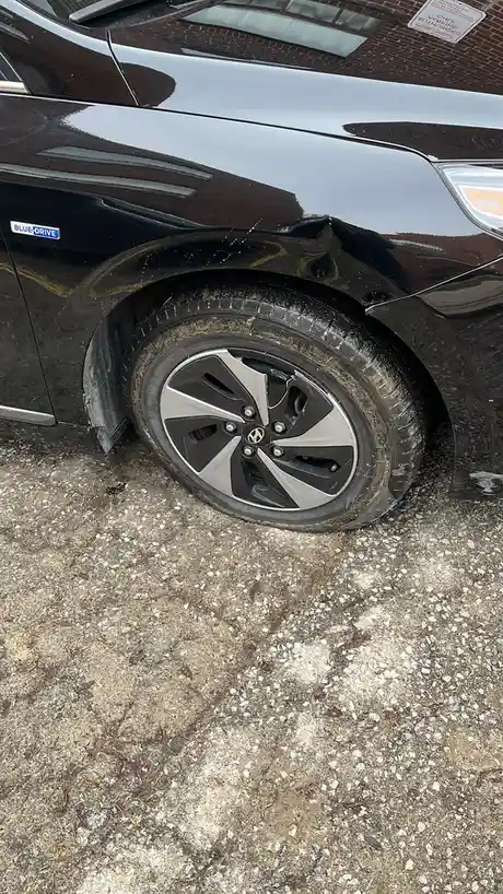 A close-up photo shows the front driver's side of a black Hyundai car, with visible mud on the wheel and fender. The car has…