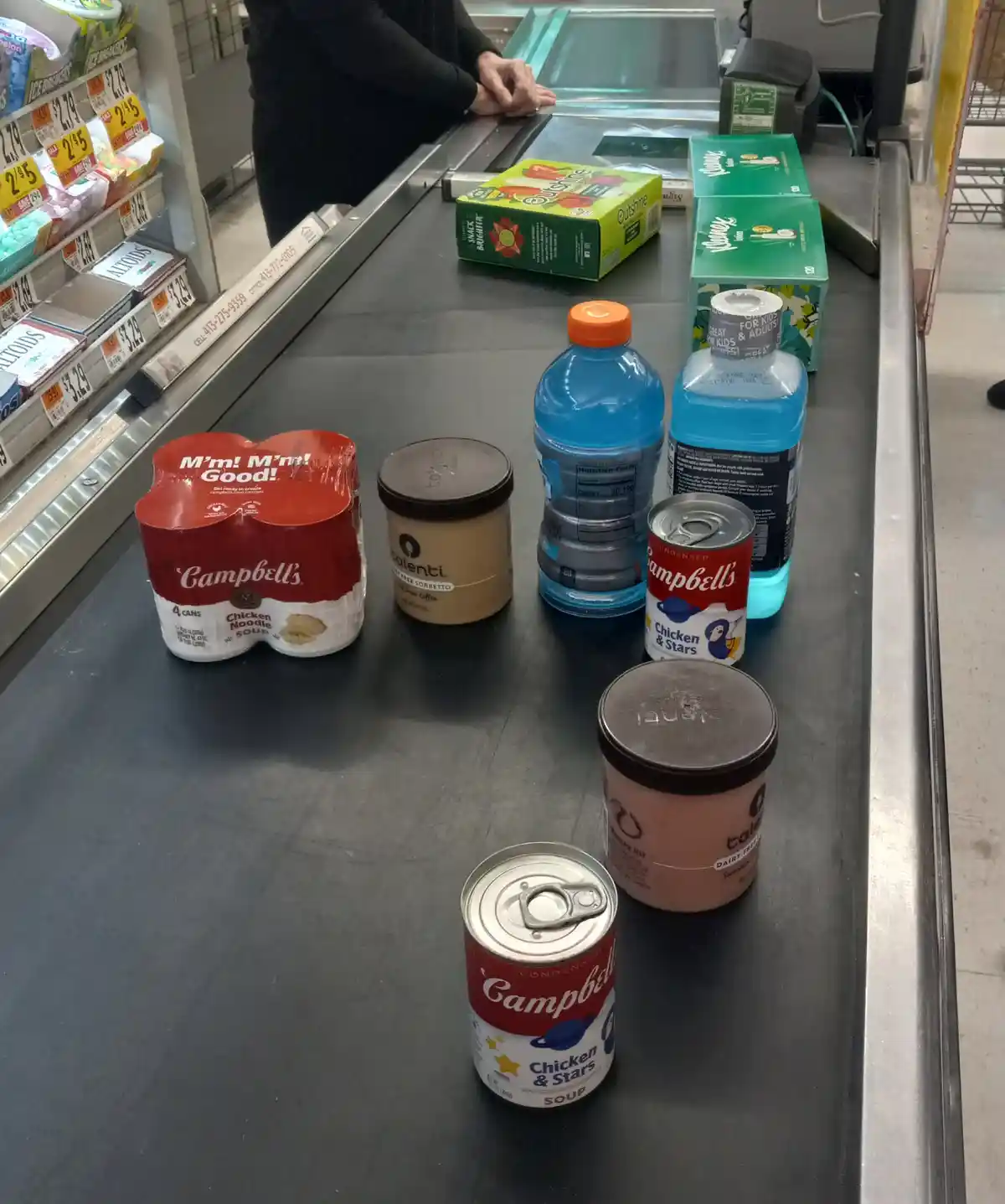 A grocery checkout counter displays several items including multiple cans of Campbell's Chicken Noodle and Chicken & Stars…