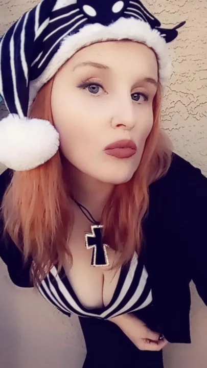 A woman with reddish hair wears a black-and-white striped sailor-style hat with a white pom-pom and a matching top. She also…