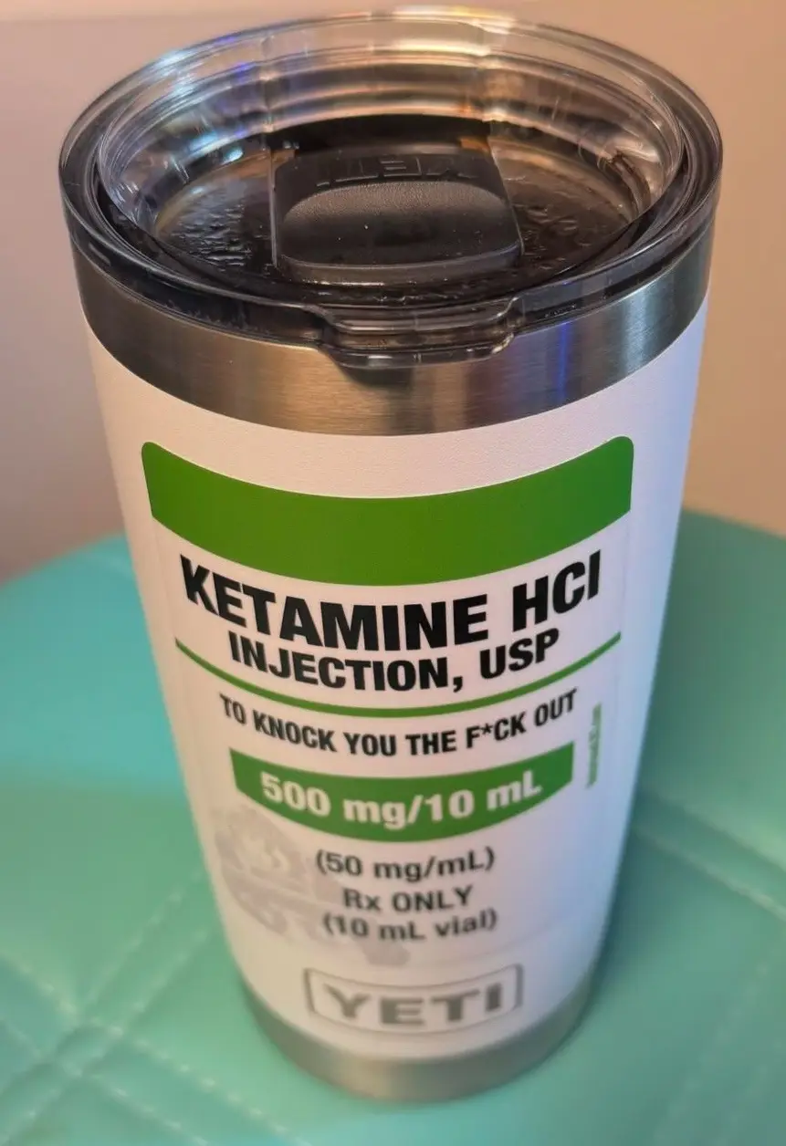A silver Yeti tumbler with a clear lid is wrapped in a label mimicking a medical vial for 'Ketamine HCl Injection, USP'…