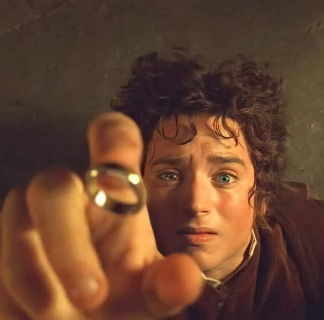 A close-up image of Frodo Baggins from 'The Lord of the Rings' holding out his hand with the One Ring, looking directly at…