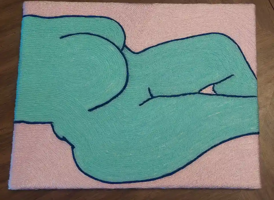 A hand-embroidered textile artwork on a pink towel background, depicting a stylized turquoise whale with a single visible…