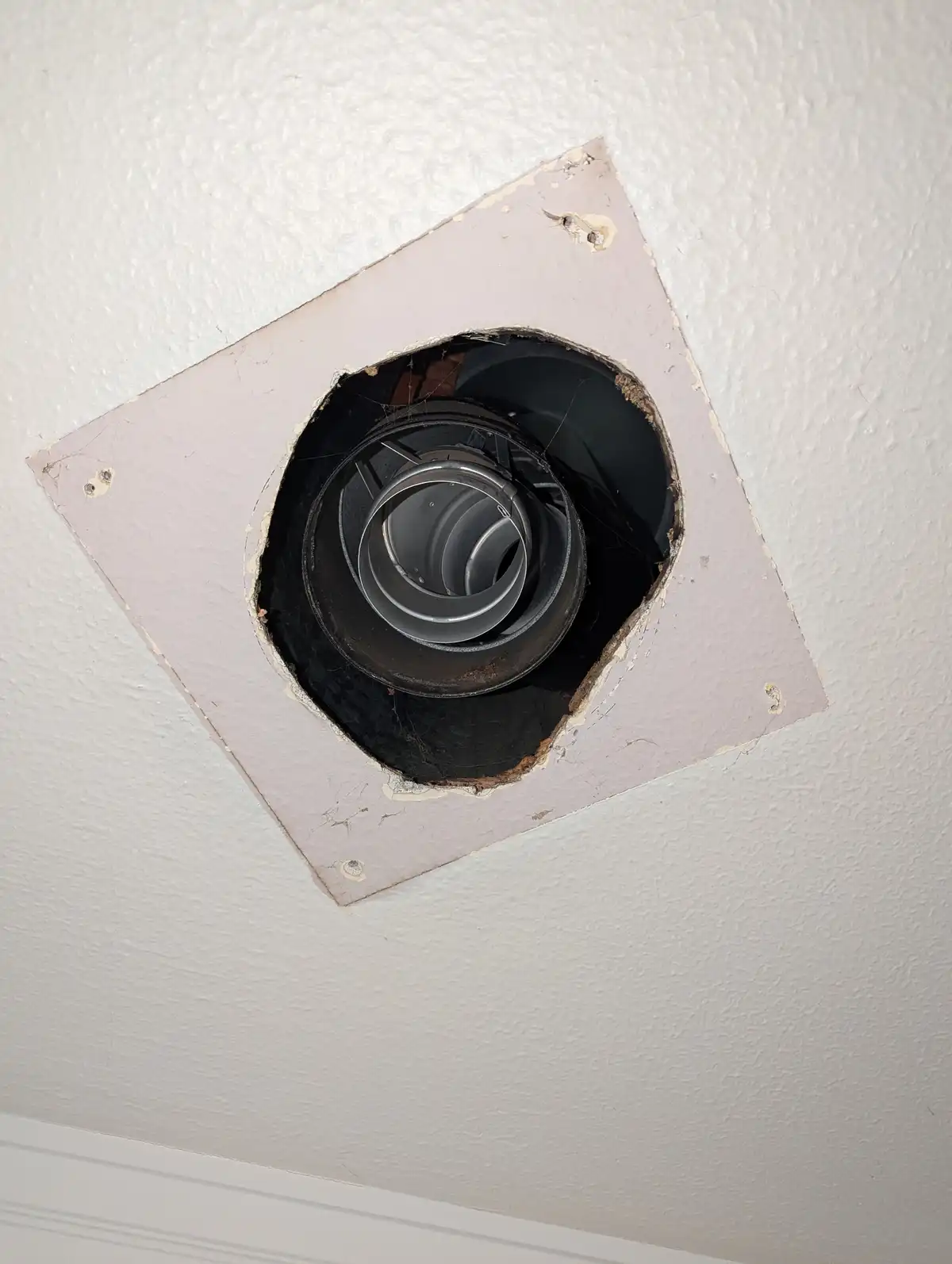 A close-up photo shows a ceiling fan's motor housing exposed through a roughly cut, square hole in a white ceiling. The…