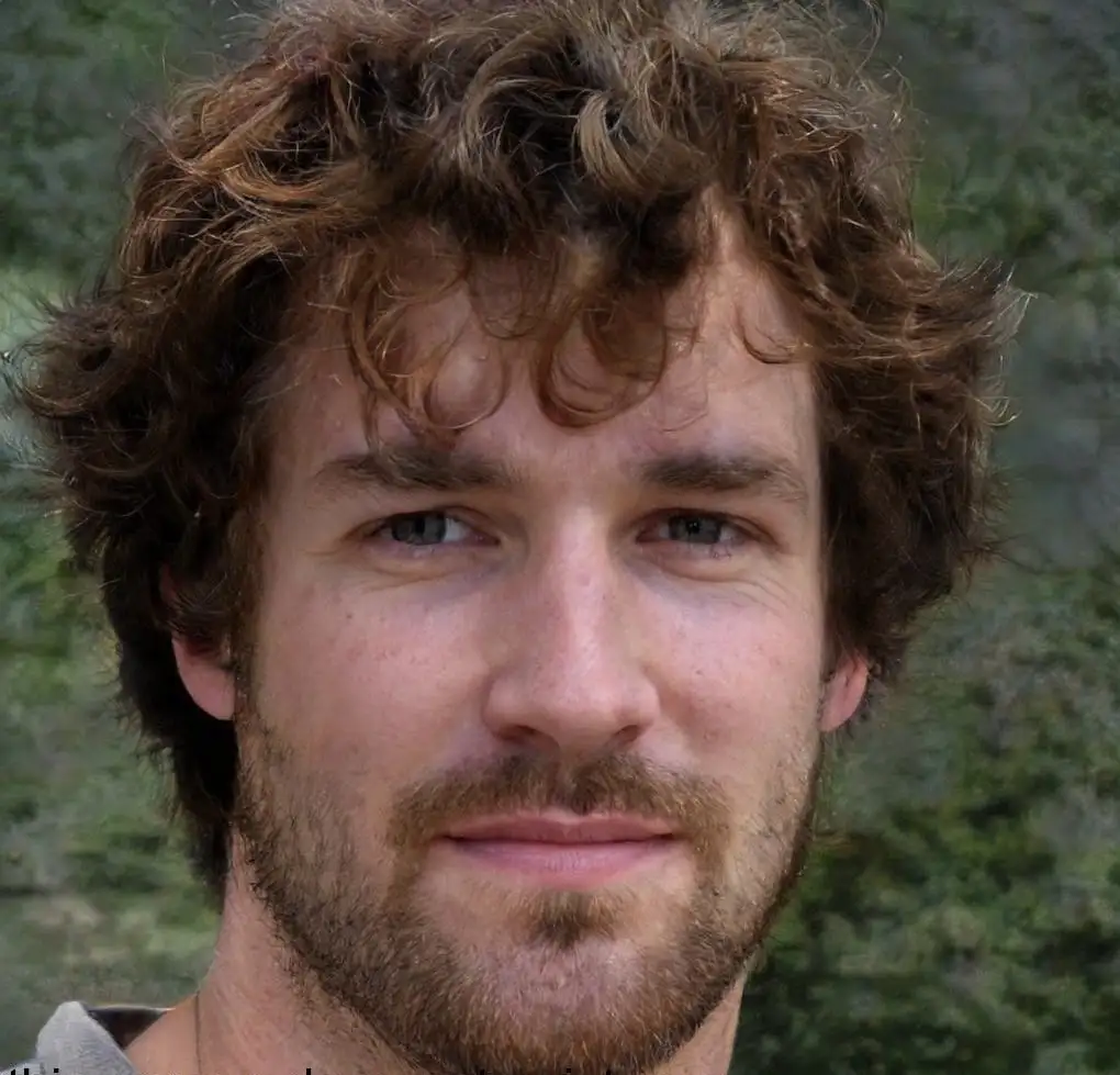 A close-up photo of a man with curly brown hair and a light beard, looking directly at the camera with a neutral expression…