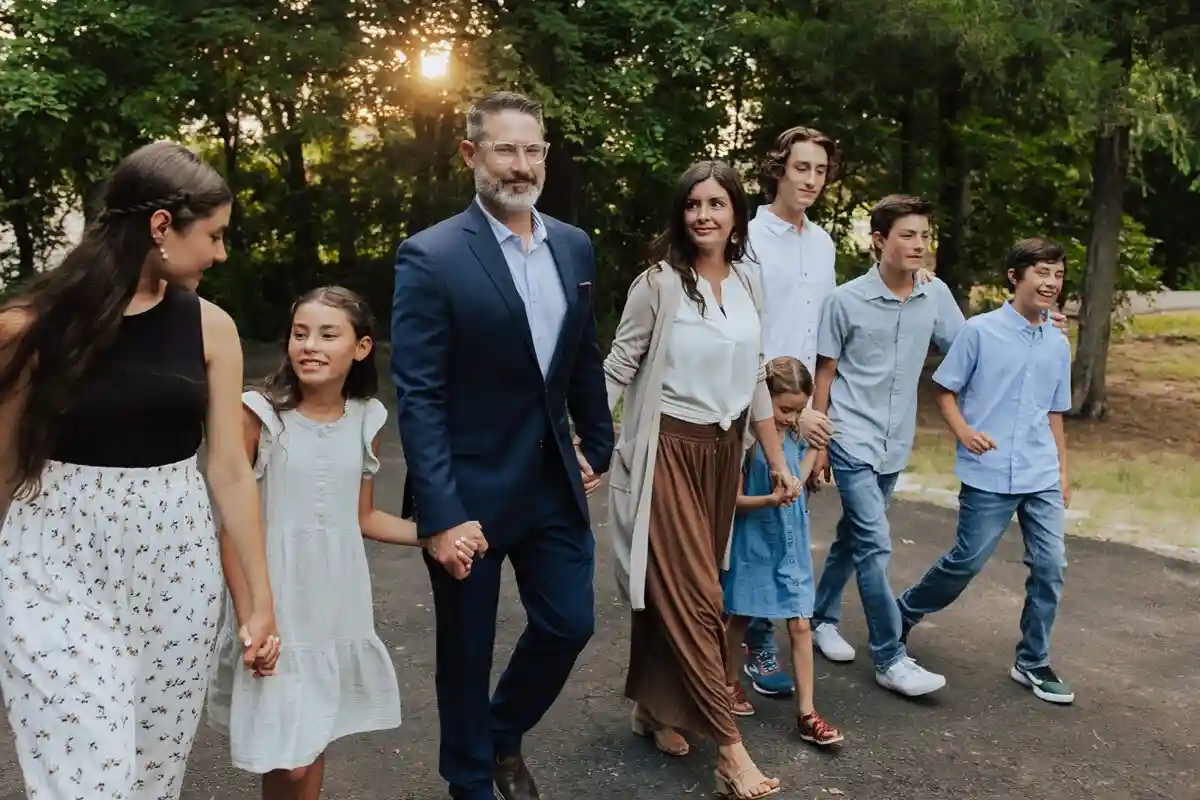 A family photo shows a man in a blue suit holding hands with a young girl, while a woman in a beige cardigan walks beside…