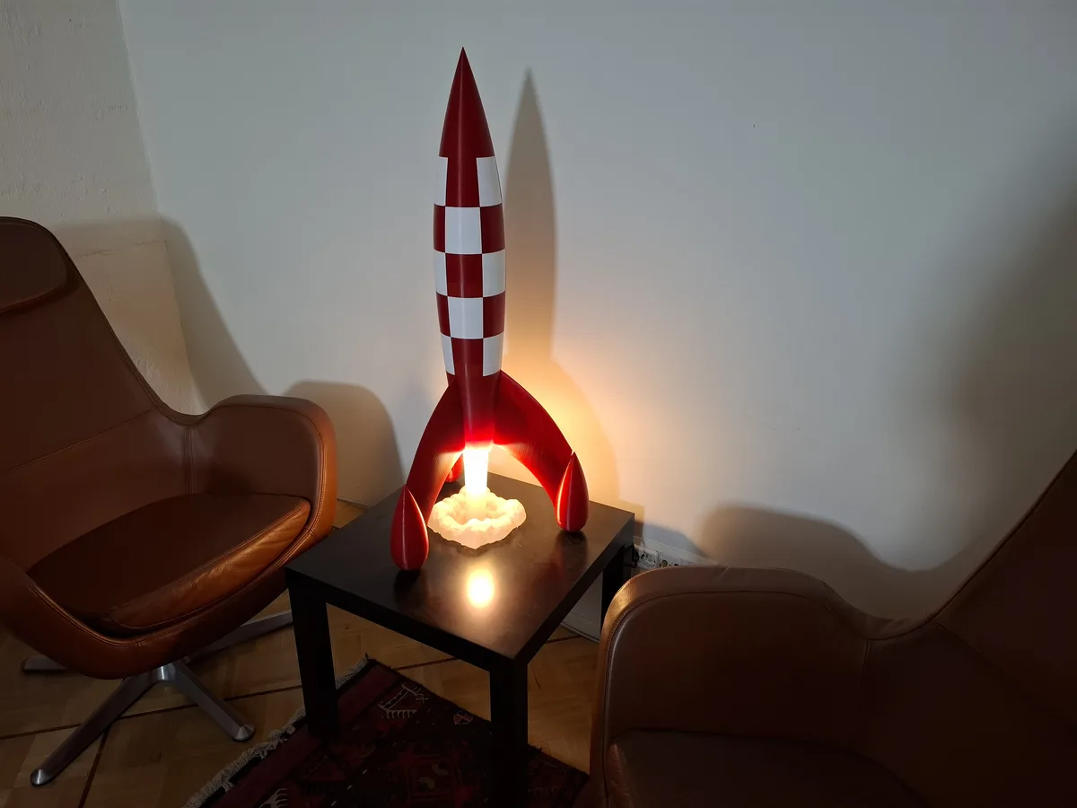 A red and white checkered rocket-shaped lamp with a glowing base sits on a small black table between two brown leather…