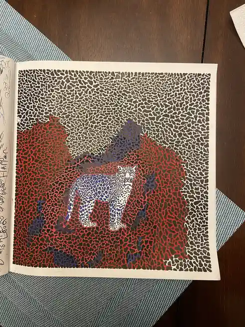 An open book displays a stylized illustration of a leopard standing amidst abstract red and blue shapes, all rendered in a…