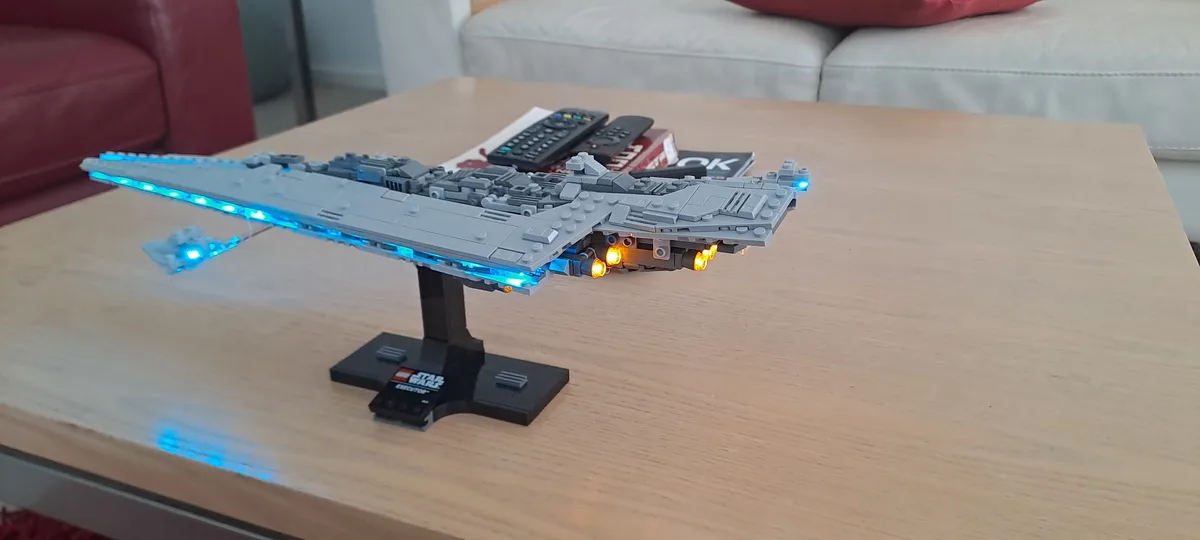 A detailed grey Lego Star Wars Executor-class Star Destroyer model with blue and orange LED lights is displayed on a black…