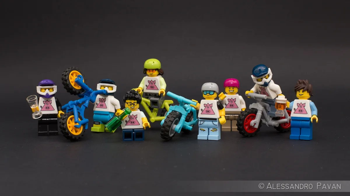 A group of LEGO minifigures, all wearing shirts with a pink pig logo, are posed with various toy motorcycles and holding…