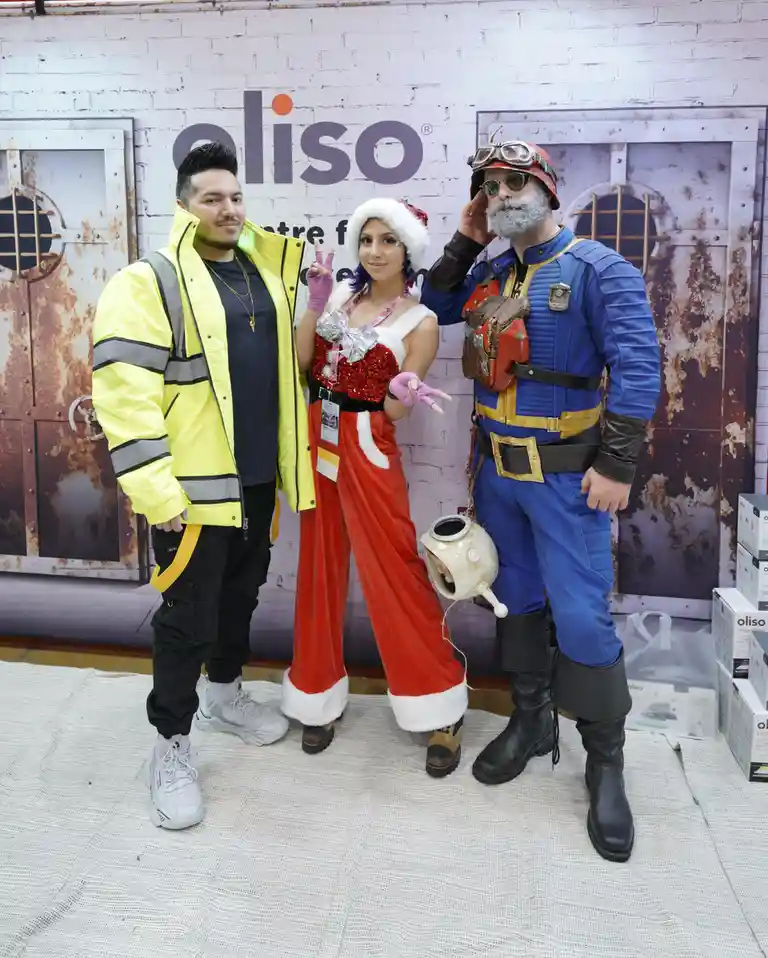 Three people pose together at an event; one wears a yellow high-visibility jacket, another a red and white Santa outfit with…