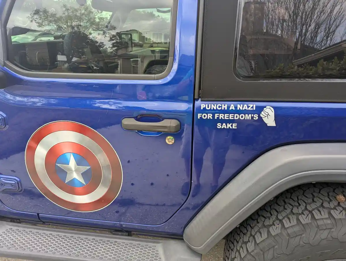 A close-up of a blue Jeep's side door shows a large Captain America shield decal and a white sticker with the text 'PUNCH A…