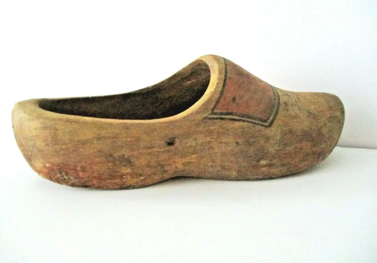 A single, worn wooden clog shoe with a reddish-brown painted patch on its side, photographed against a plain white…