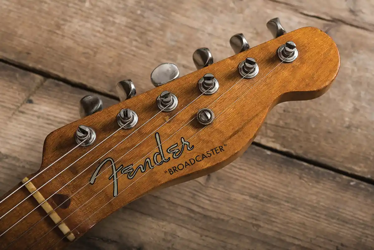 A close-up photograph of a vintage Fender guitar headstock, showing the 'Fender' logo and 'BROADCASTER' model name in…