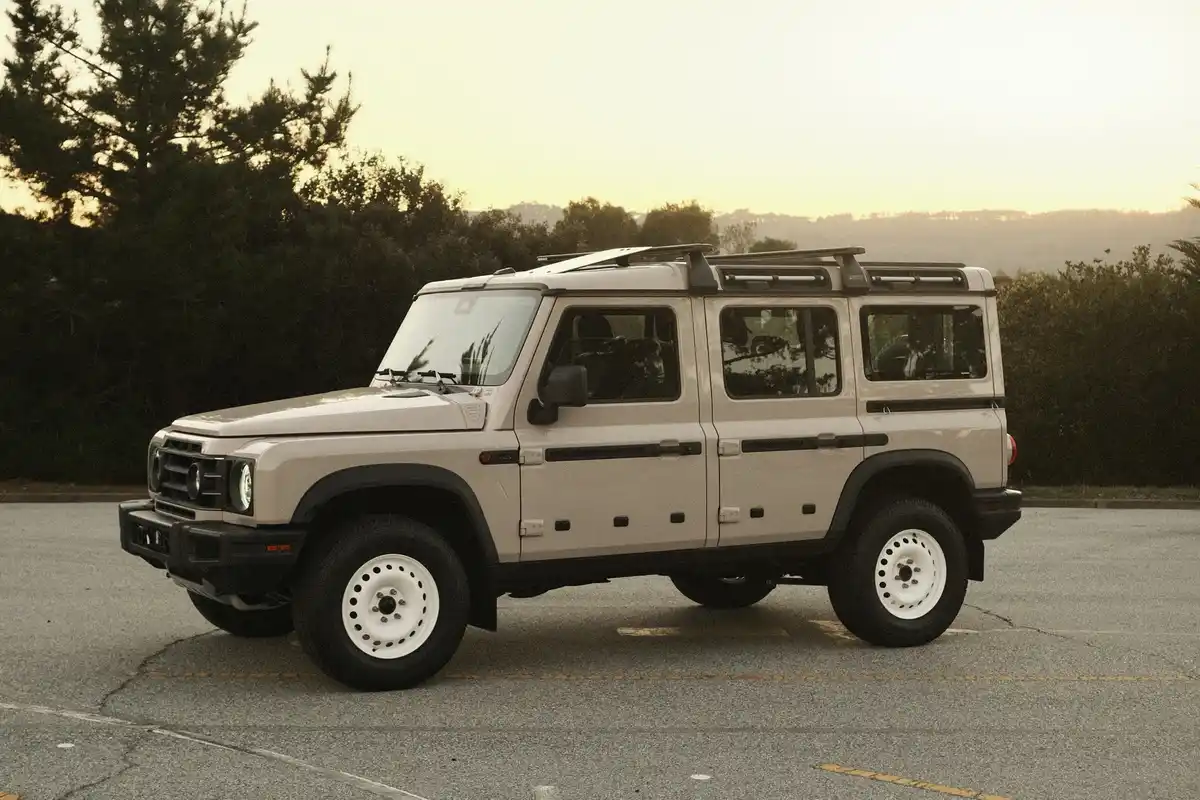 A beige, boxy, four-door SUV with white wheels and a roof rack is parked in a lot at sunset. The overlaid text reads 'i'm…