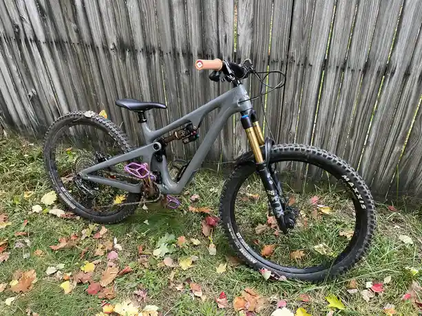 A grey full-suspension mountain bike with gold front forks and purple pedals is parked on grass with fallen autumn leaves…