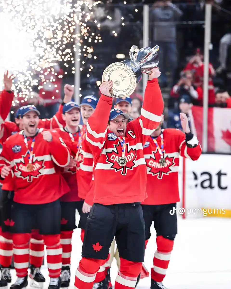 A jubilant Canadian ice hockey player, wearing a red jersey with a maple leaf and a 'C' for captain, holds up a large silver…