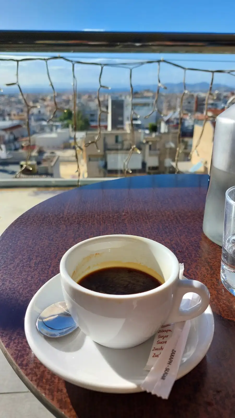 A white espresso cup with a small amount of dark coffee sits on a saucer with a spoon and sugar packets on a speckled table…