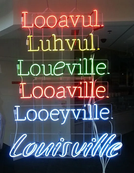 A vertical neon sign displays the name 'Louisville' in blue cursive at the bottom, with six misspellings above it in…