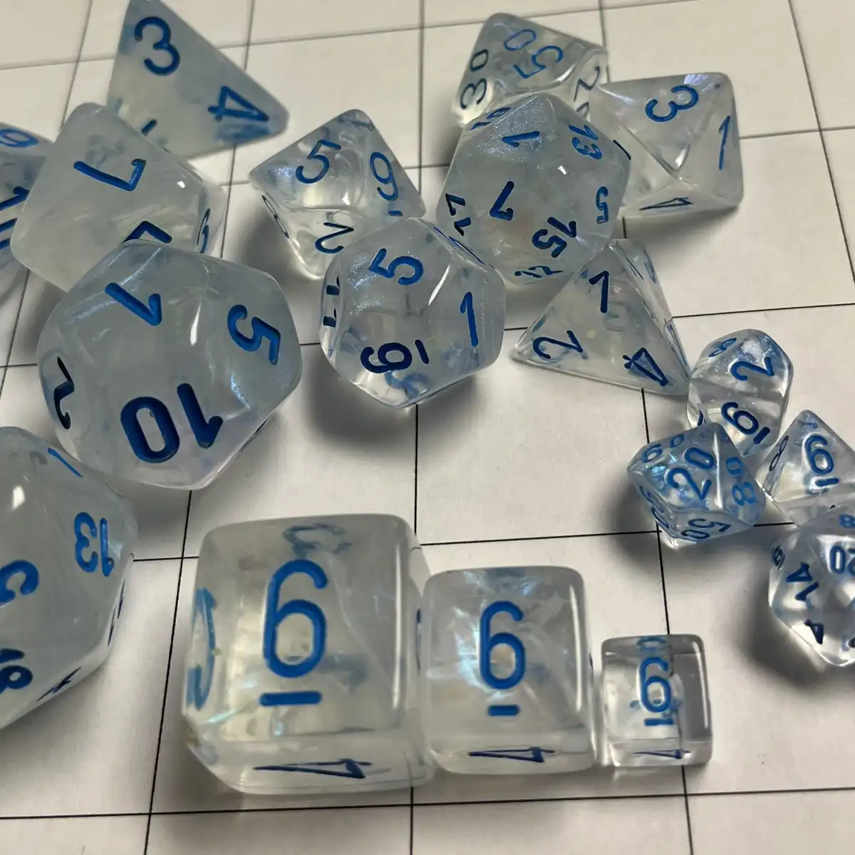 A collection of translucent, blue-numbered polyhedral dice are scattered across a white tiled surface. Several dice show…