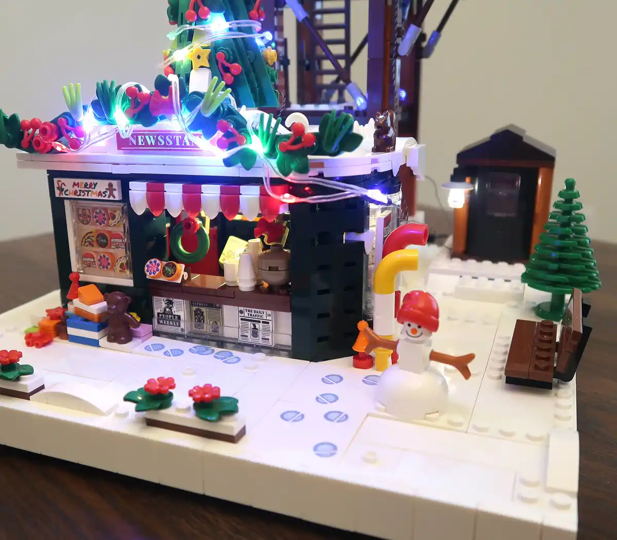 A detailed LEGO Christmas scene features a newsstand decorated with colorful lights, holly, and a 'MERRY CHRISTMAS' sign…