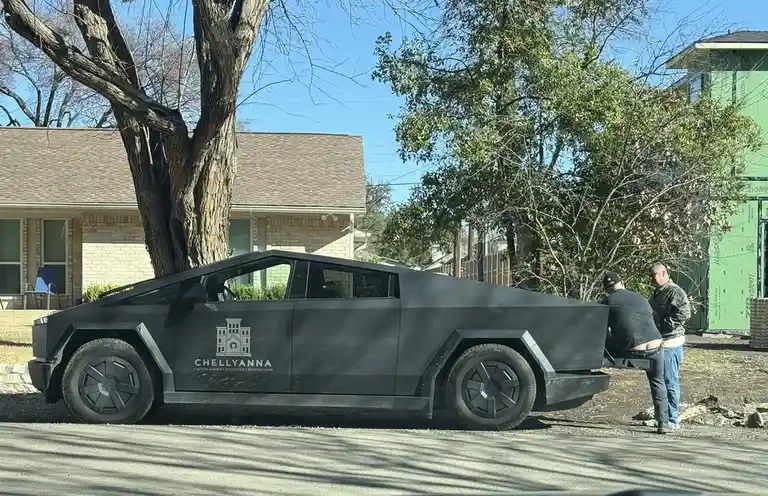 A matte black Tesla Cybertruck is parked on a residential street with a logo for 'Chellyanna Custom Homes Additions…