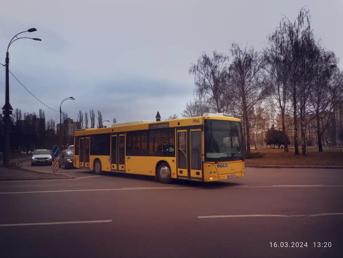 A yellow public bus, number 7816, is shown on a city street with bare trees and overcast skies. The bus's destination sign…