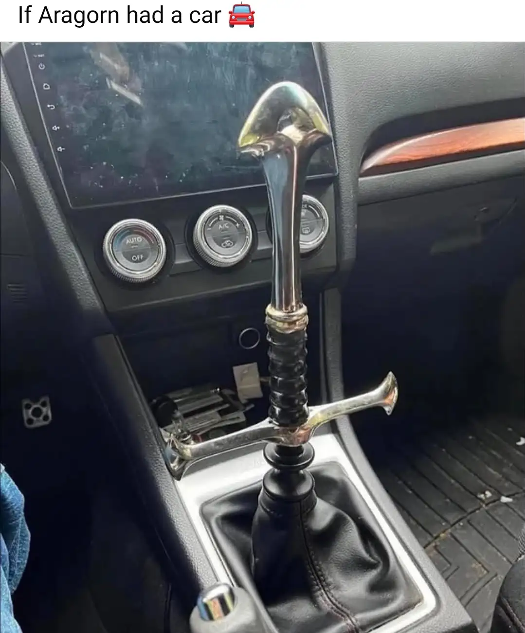 A close-up photo of a car's center console shows a sword, specifically a replica of Aragorn's sword Anduril, inserted into…