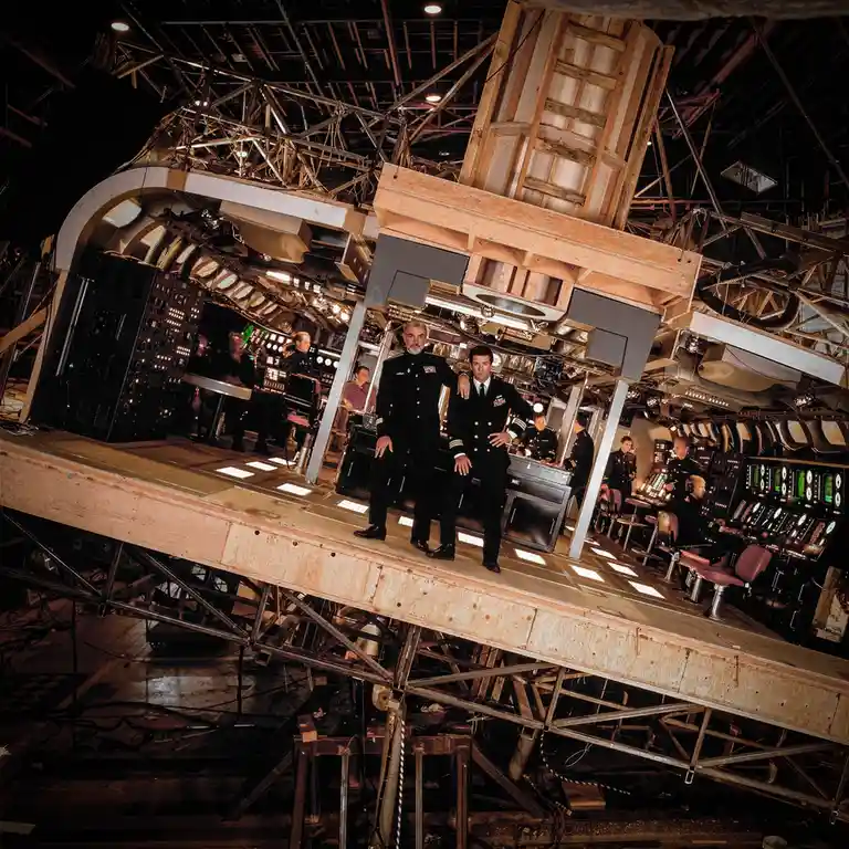 A behind-the-scenes photo from the Star Trek movie set, showing actors in naval uniforms posing confidently on a tilted…