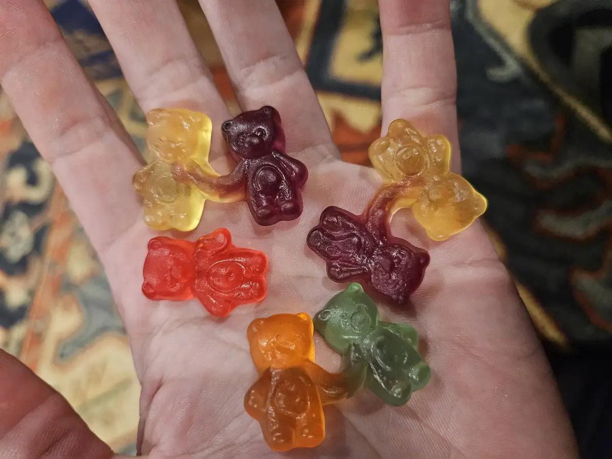 A person's open palm holds several colorful gummy bears, some of which are fused together in pairs. The overlaid text reads…