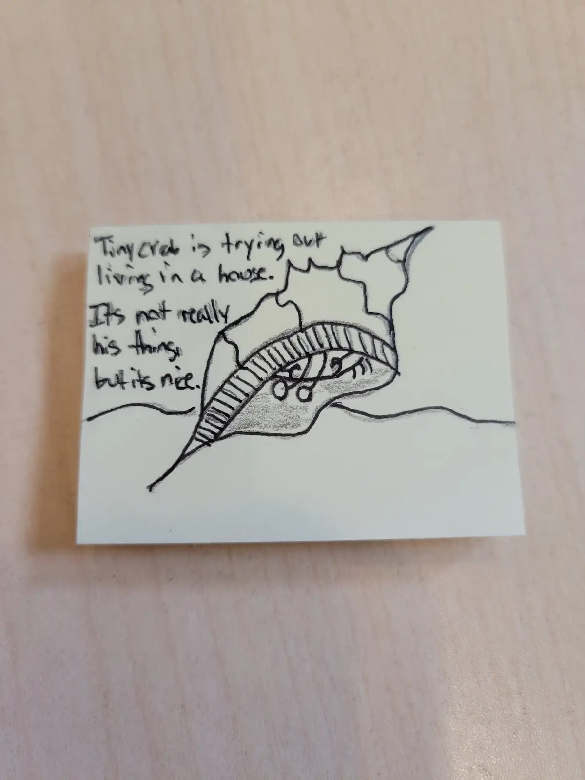 A hand-drawn sketch on a white sticky note shows a small crab inside a seashell that is drawn to resemble a house with a…