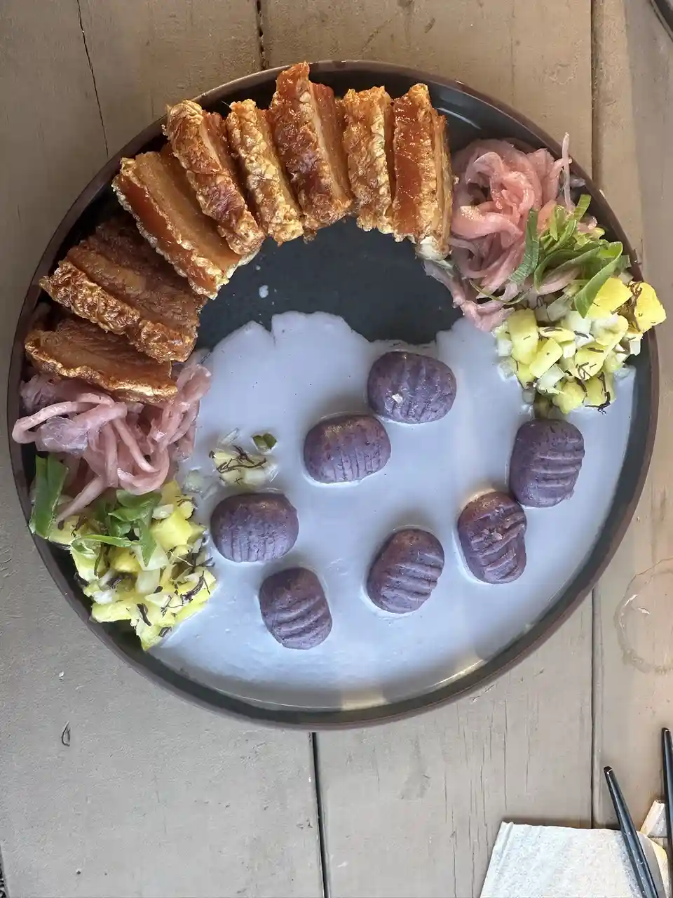 An overhead photo of a dark bowl containing a white, creamy base with seven purple, ridged dumplings arranged in a circle…