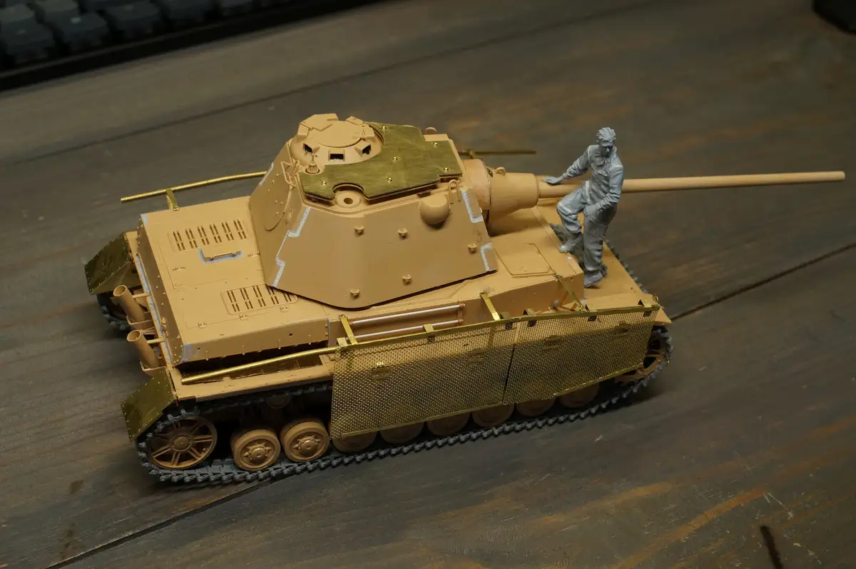 A scale model of a German Tiger tank, mostly painted tan, with numerous gold-colored metal parts including the front grill…