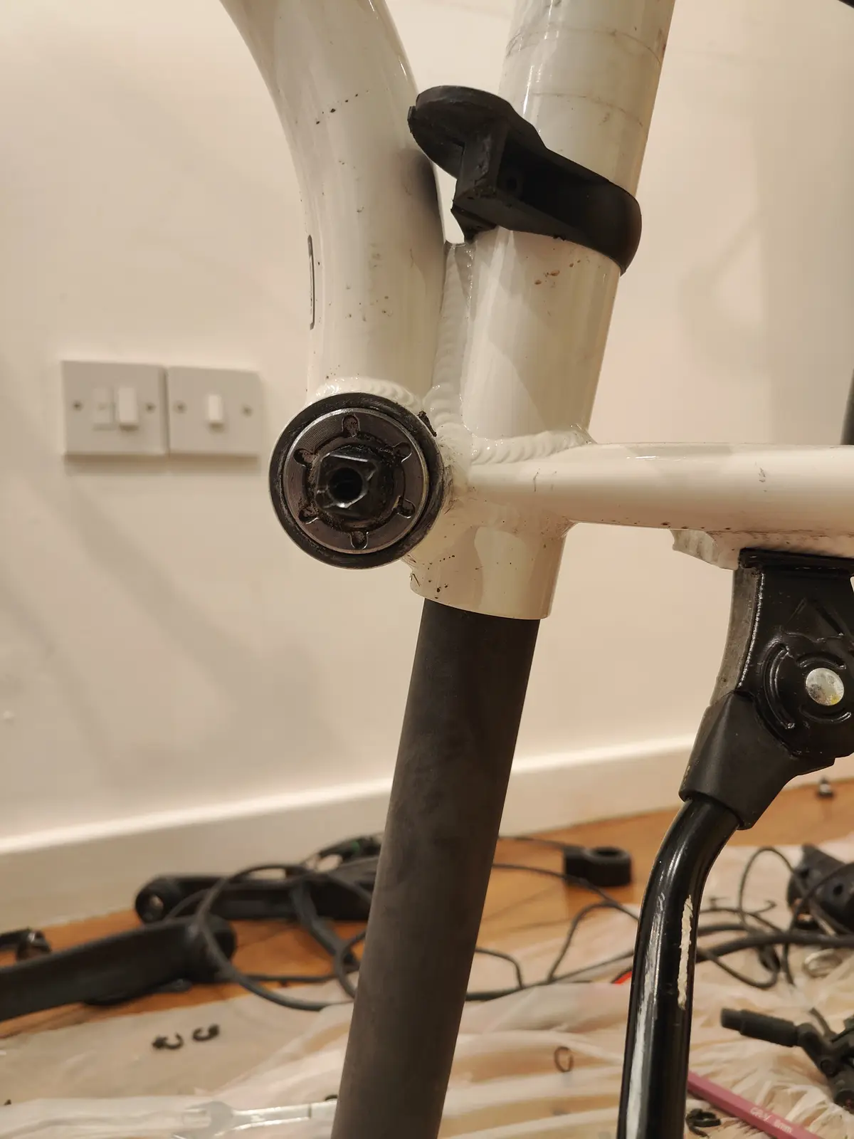 A close-up photo of a white bicycle frame with a black fork, showing a hexagonal bolt head at the front. The background…